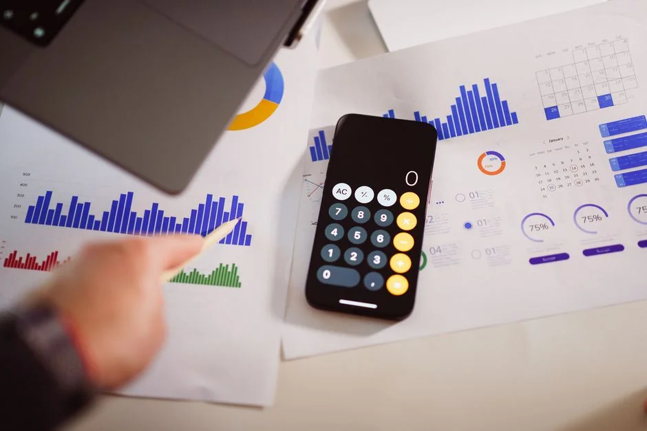 Two businessmen analyze stock market data using a smartphone and laptop in a modern office setting.